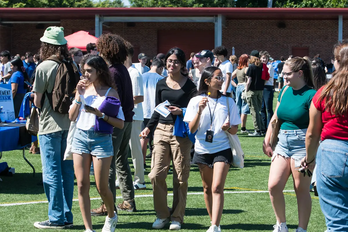 Young women wander through a field at the Engagement Fair crowded with other students