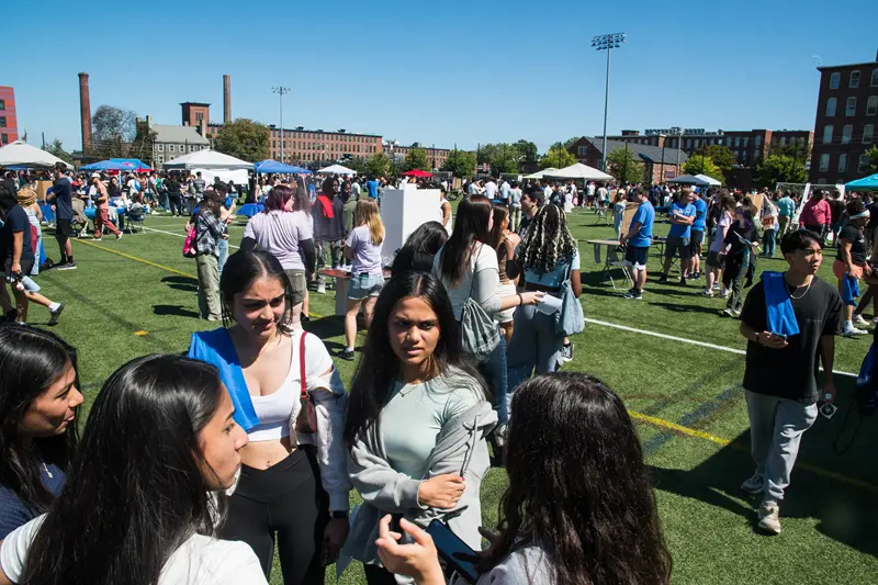 5 young women chatting in a circle in the foreground with umbrellas and hundreds of people in background