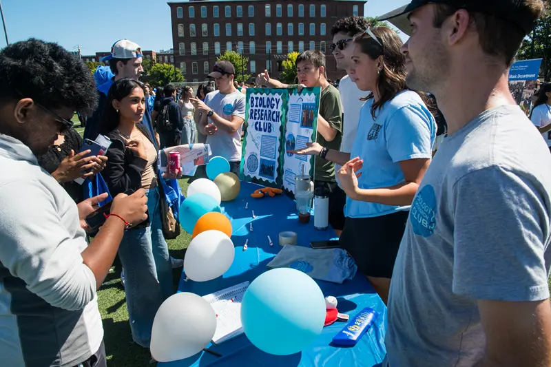 Students gather around a table with balloons on it and a poster that says Biology Research Club