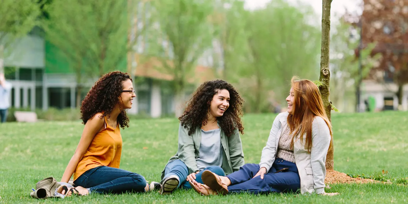 Three female students sit on the south lawn
