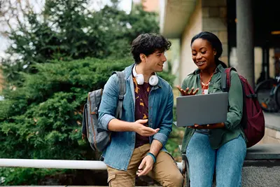 Two students looking and gesturing at a laptop computer