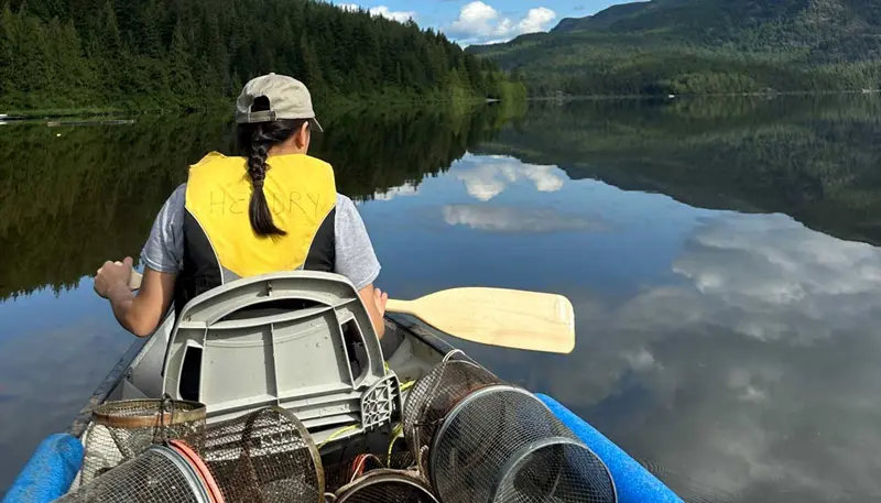 Annie Cary canoes in a lake surrounded by mountains while wearing a life jacket and holding a paddle.