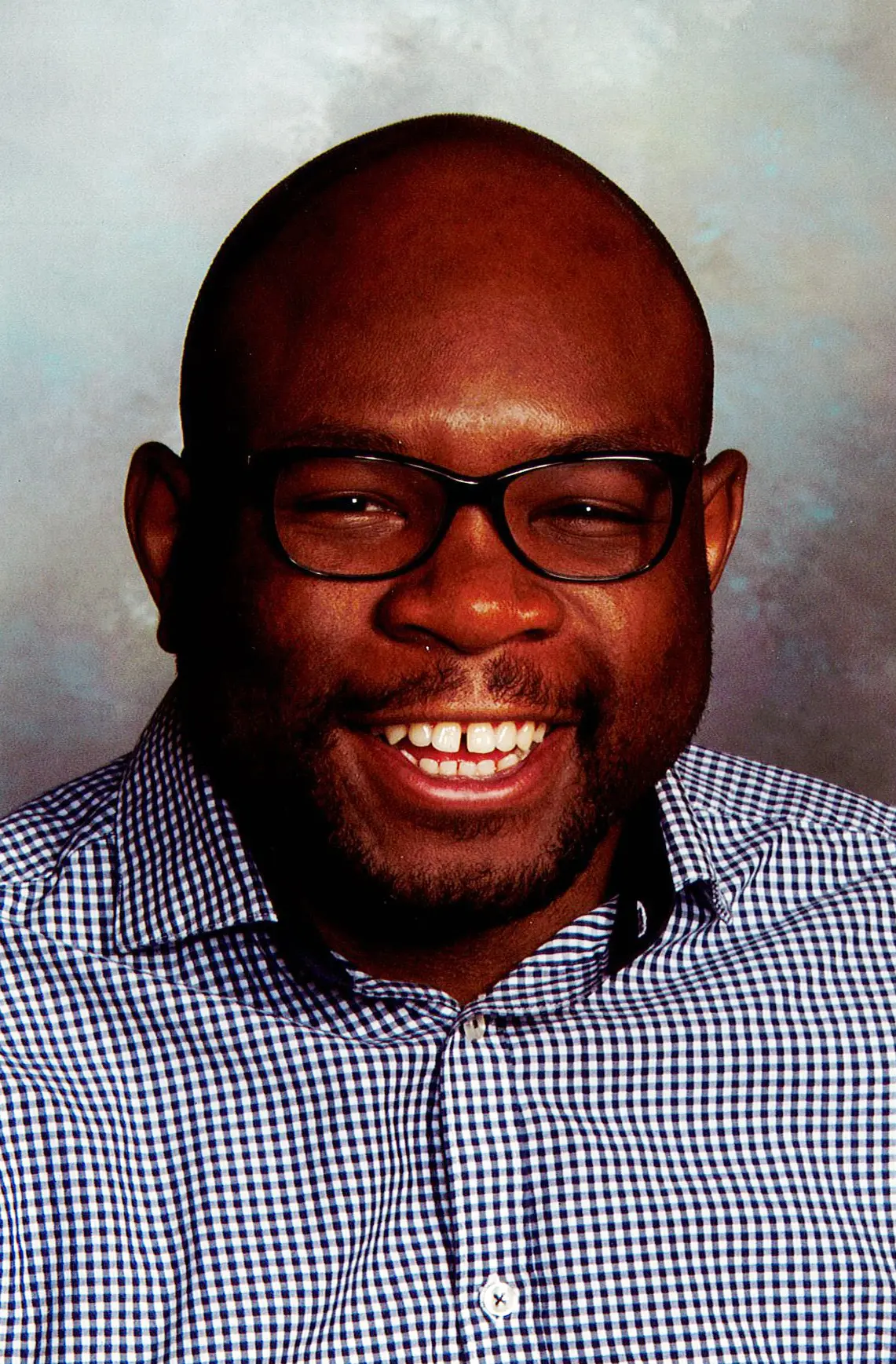 A person wearing glasses and a checkered shirt smiling.