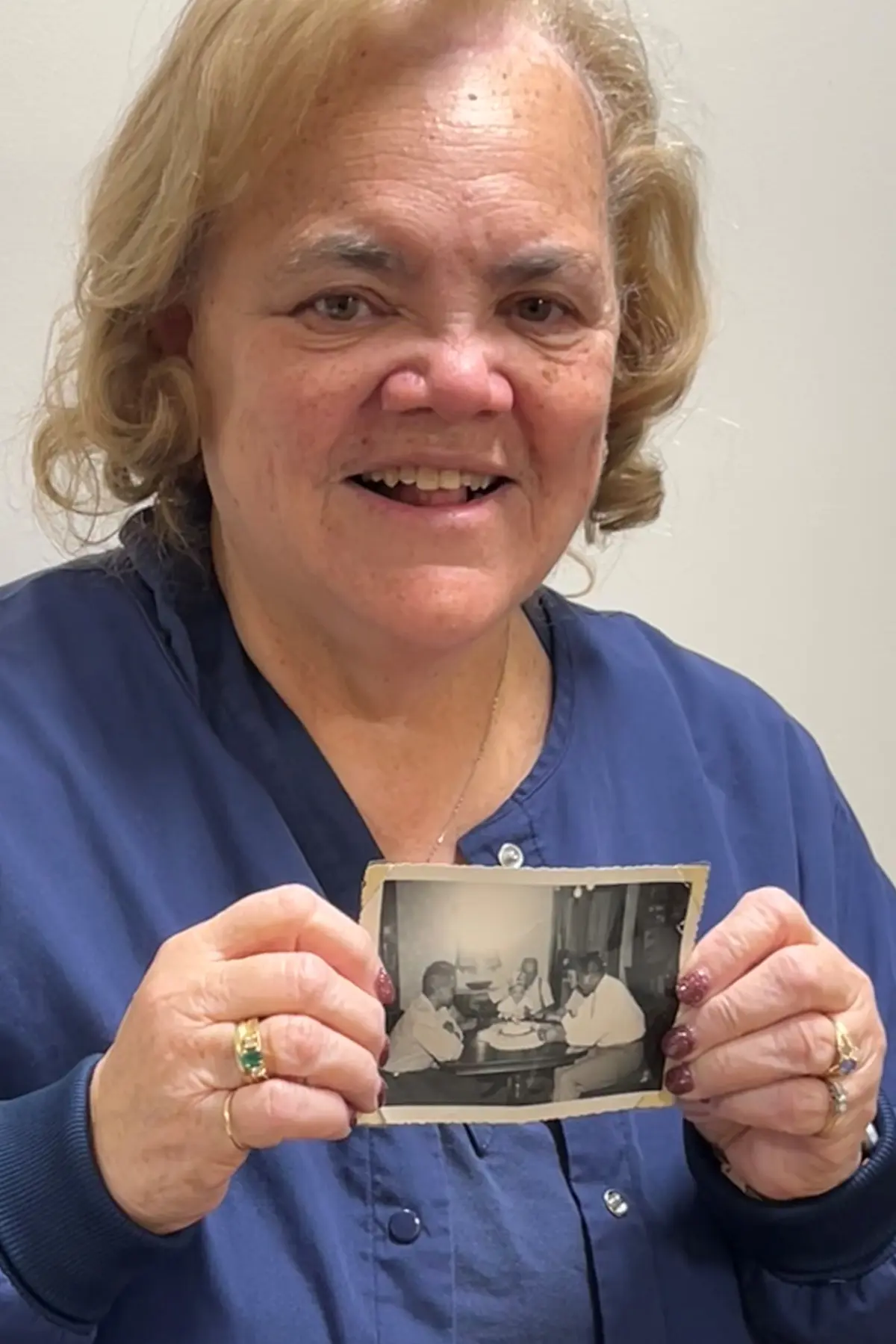 A woman smiles for a picture while holding an old black and white photograph