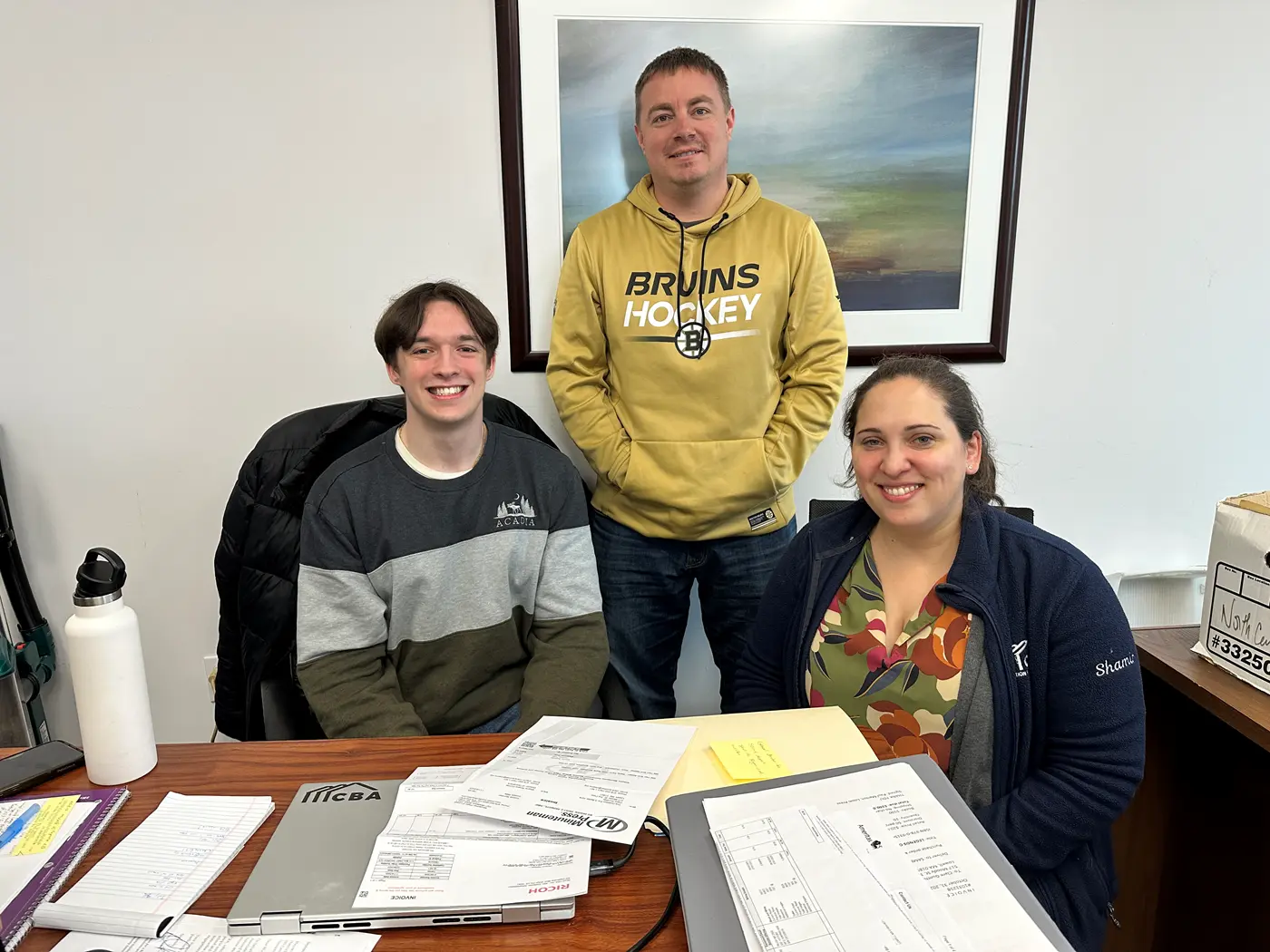 Honors student Aidan Riker sits at a desk, flanked by his supervisors at Coalition for a Better Acre