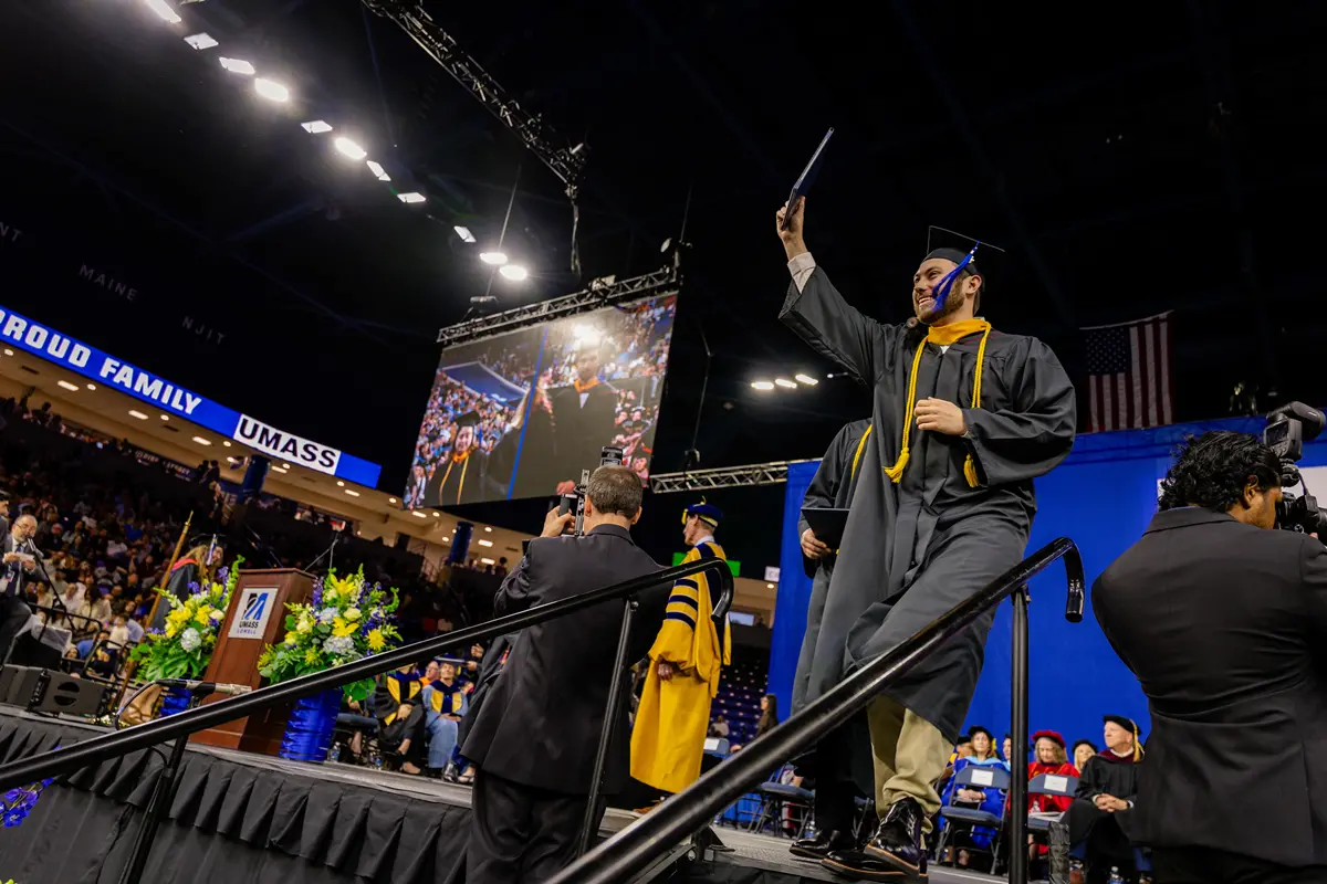 Student dressed in academic regalia lifts a diploma on the stage during a commencement ceremony 