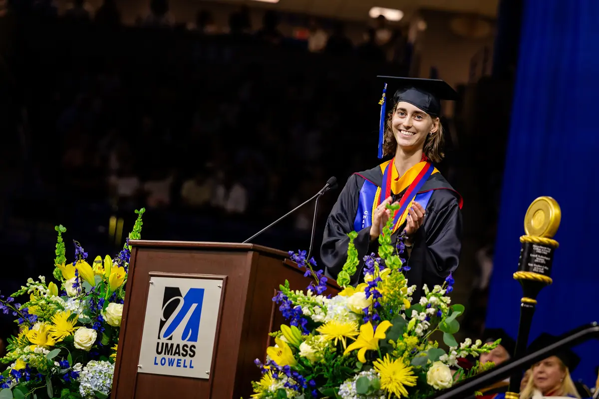 A graduate dressed in academic regalia stands behind a podium during a commencement ceremony