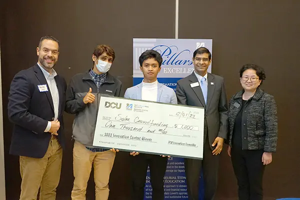 Five people pose for a photo while holding a giant check
