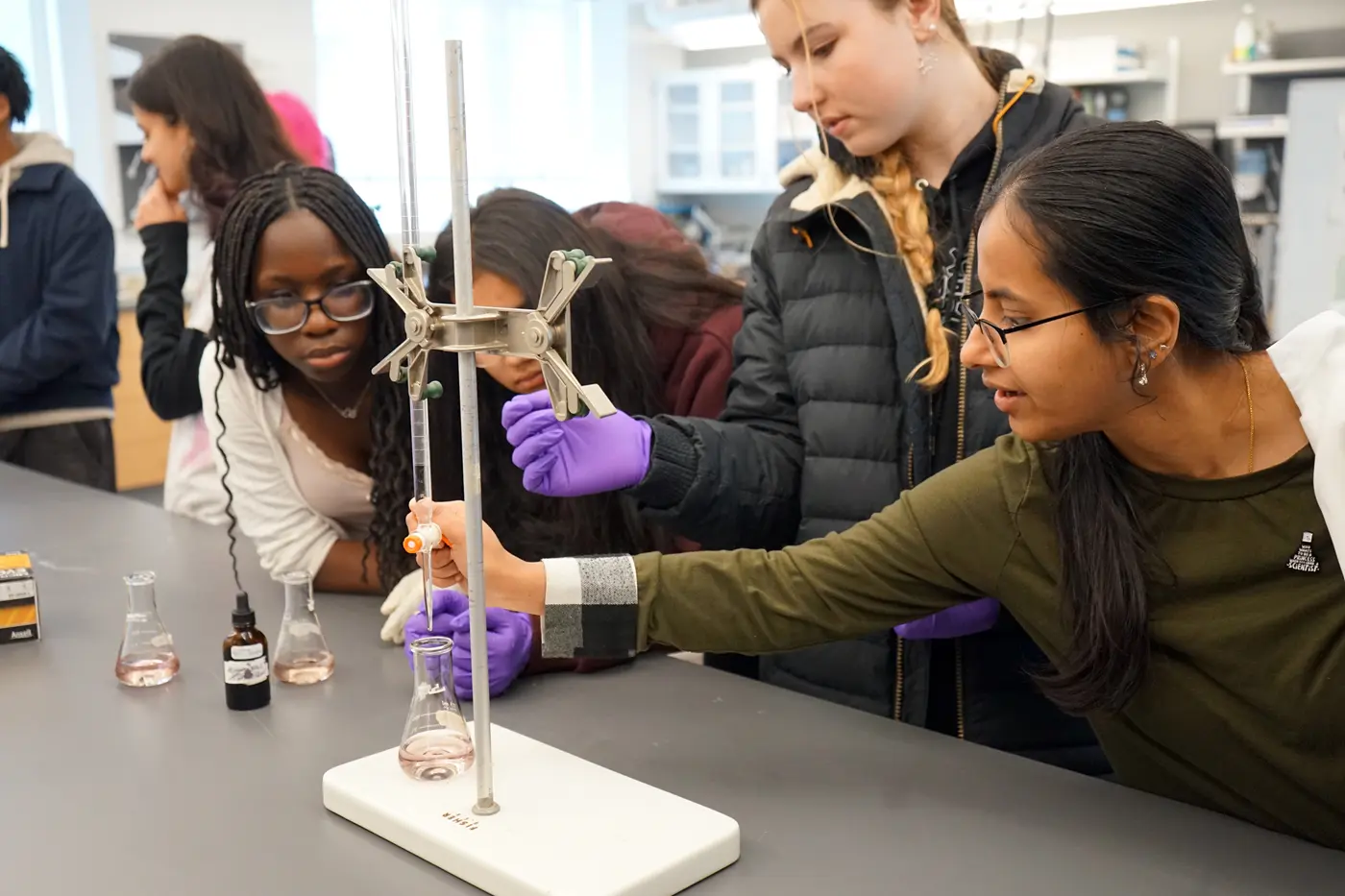 Four young women surround a beaker on a science lab workbench.