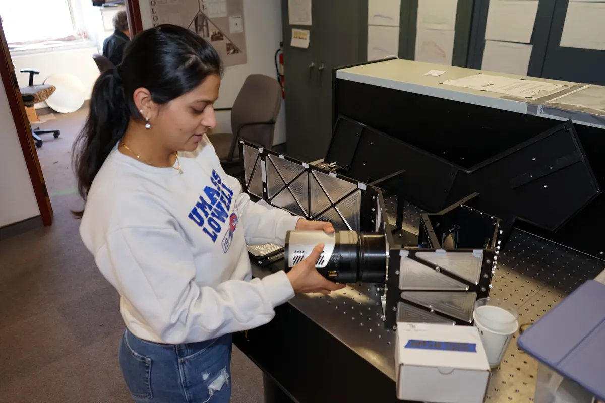 A young woman in a white sweatshirt holds a piece of an optical instrument.