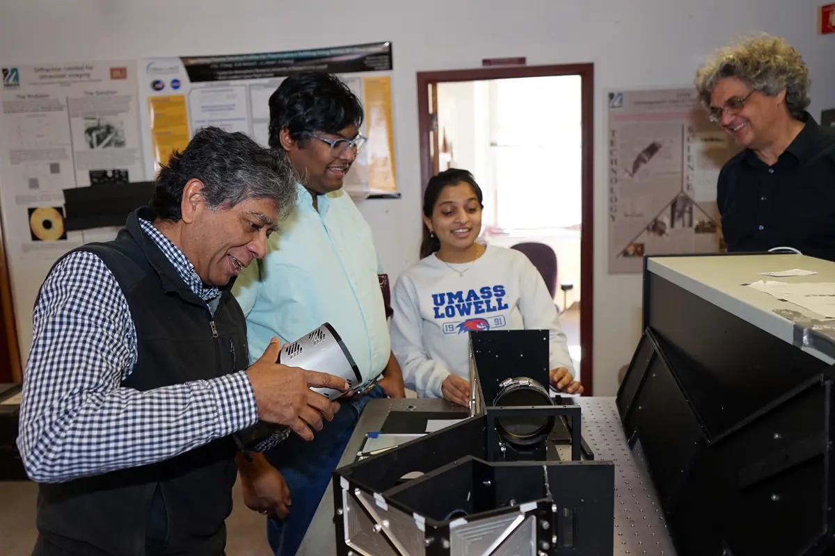 Three men and a woman stand around an optical instrument in a room and talk.
