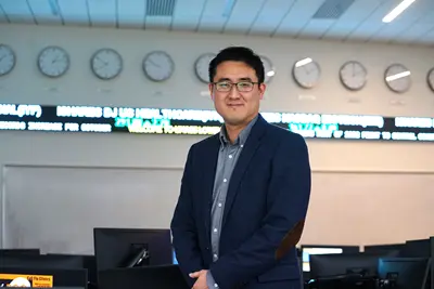 A man with glasses and wearing a blazer poses for a photo in a classroom.