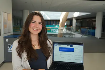 A young woman poses for a photo while holding a laptop.