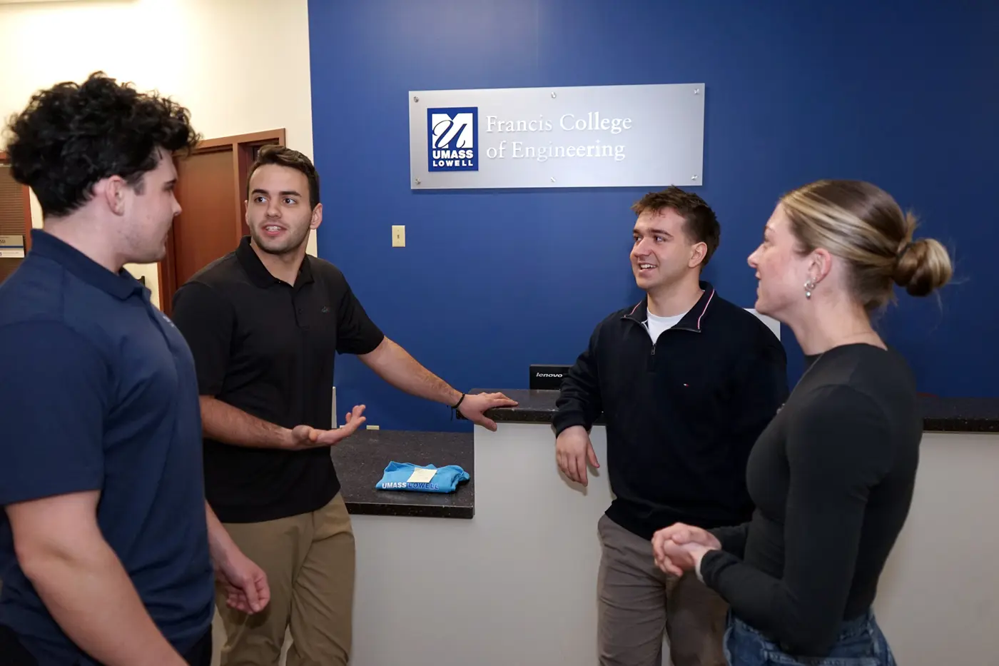 Three young men and a young woman stand in a circle and talk in the reception area of an engineering college.