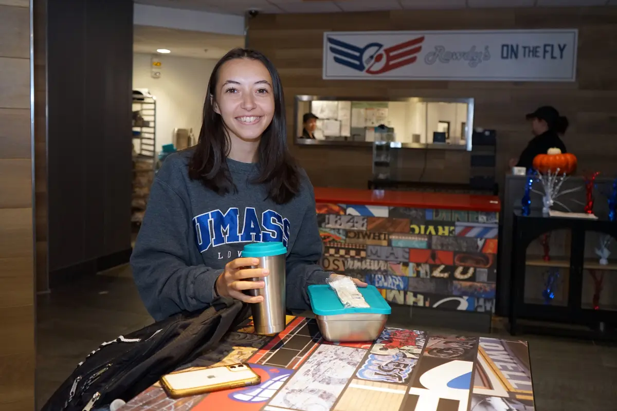 A young woman poses for a photo while holding a metal reusable cup and food container.