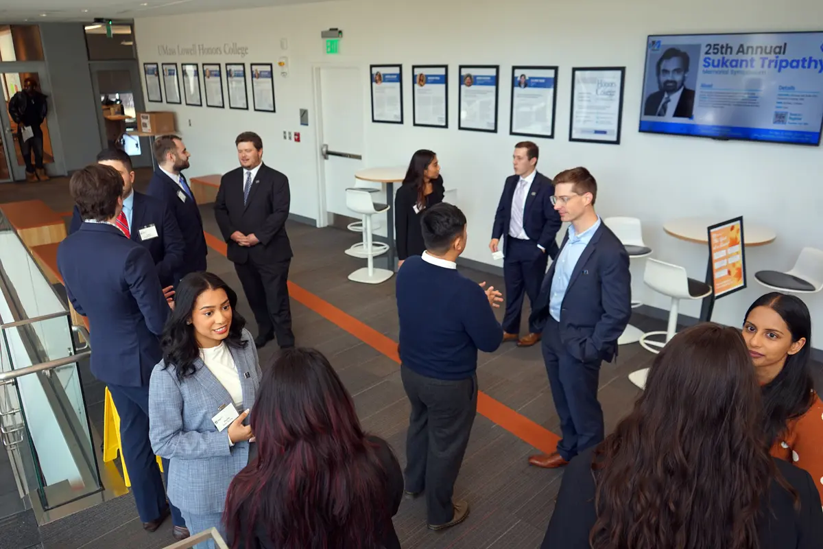 Men and women in business attire mingle and talk in a hallway.