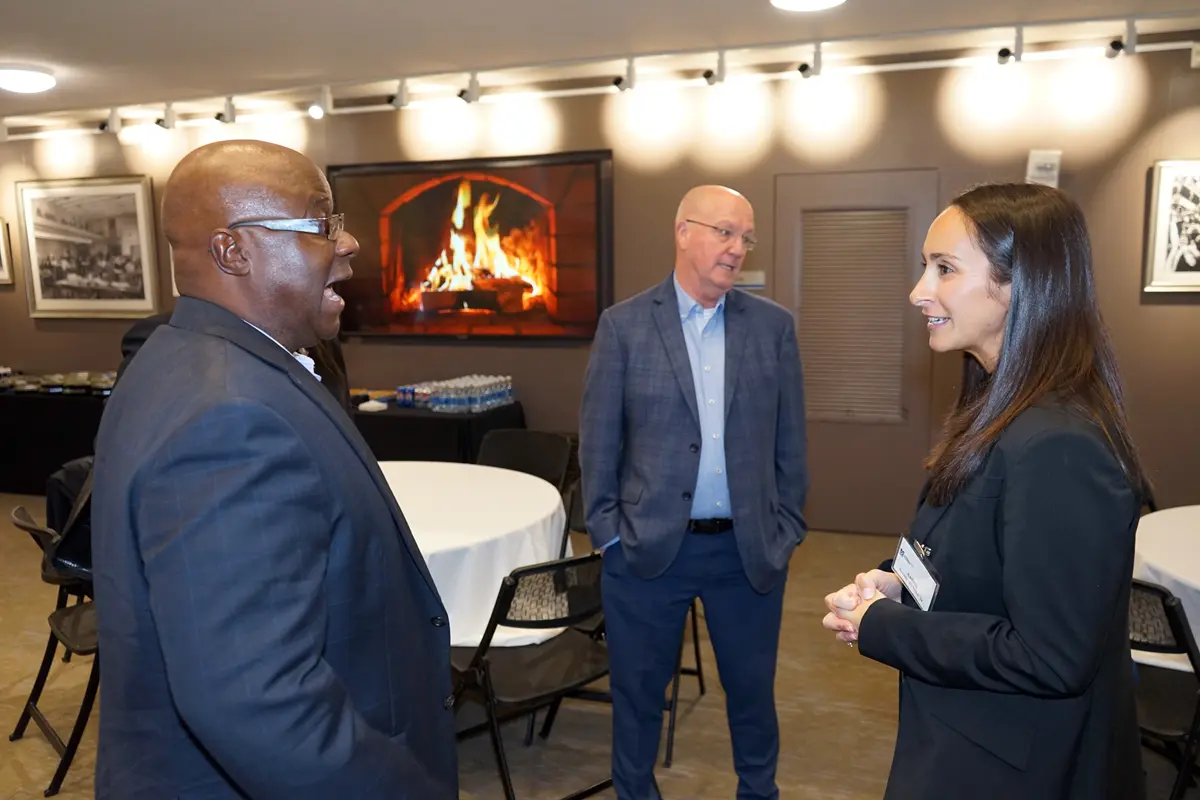 A man and a woman talk while another man stands in the background.