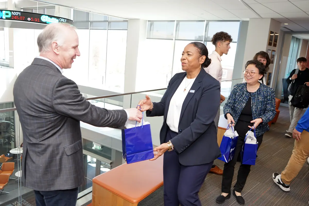 A person hands a person in a suit a blue gift bag.