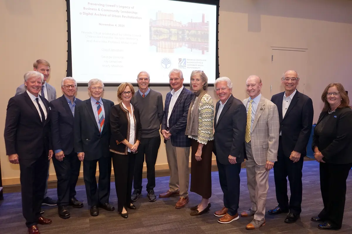 A dozen people pose for a group photo standing in front of a screen.