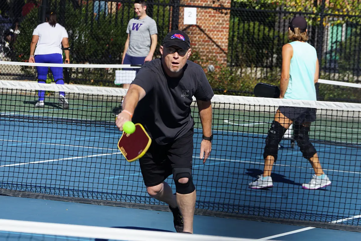 Two women in visors and sun glasses smile while holding pickleball paddles outside.
