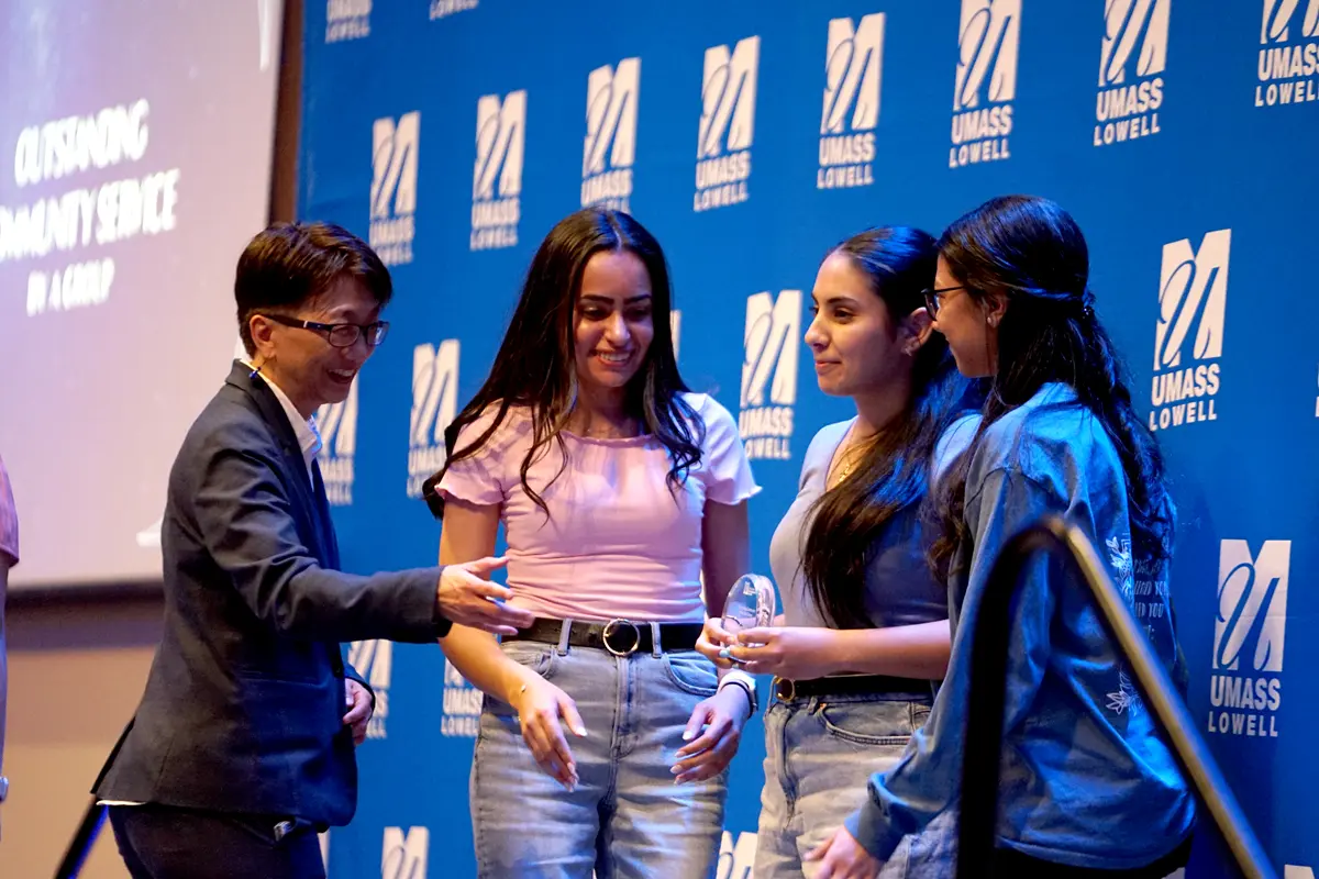 A woman with glasses presents an award to three young women on a stage.