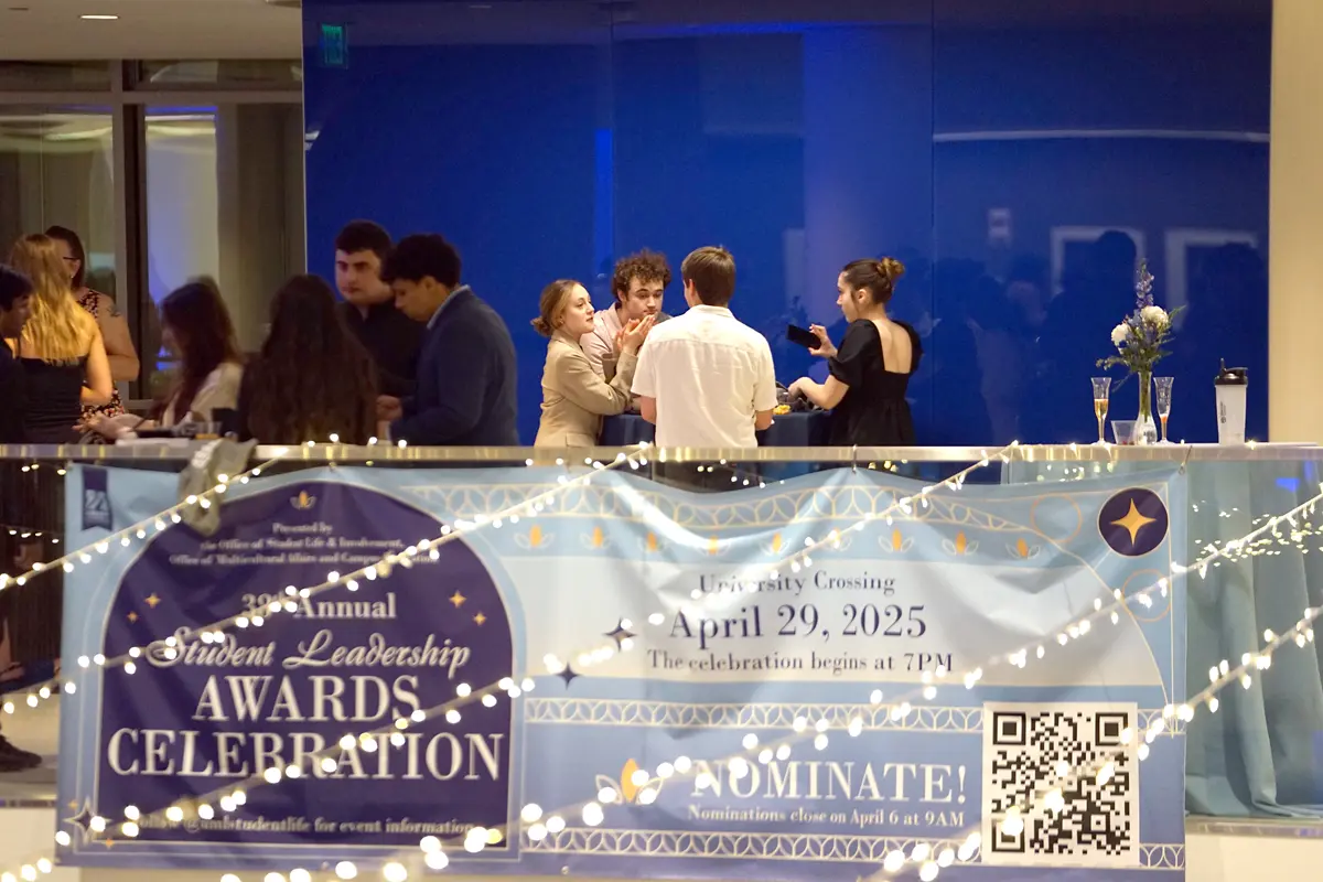 Several students chat while standing on a balcony, which has a banner for an awards ceremony hanging from it.