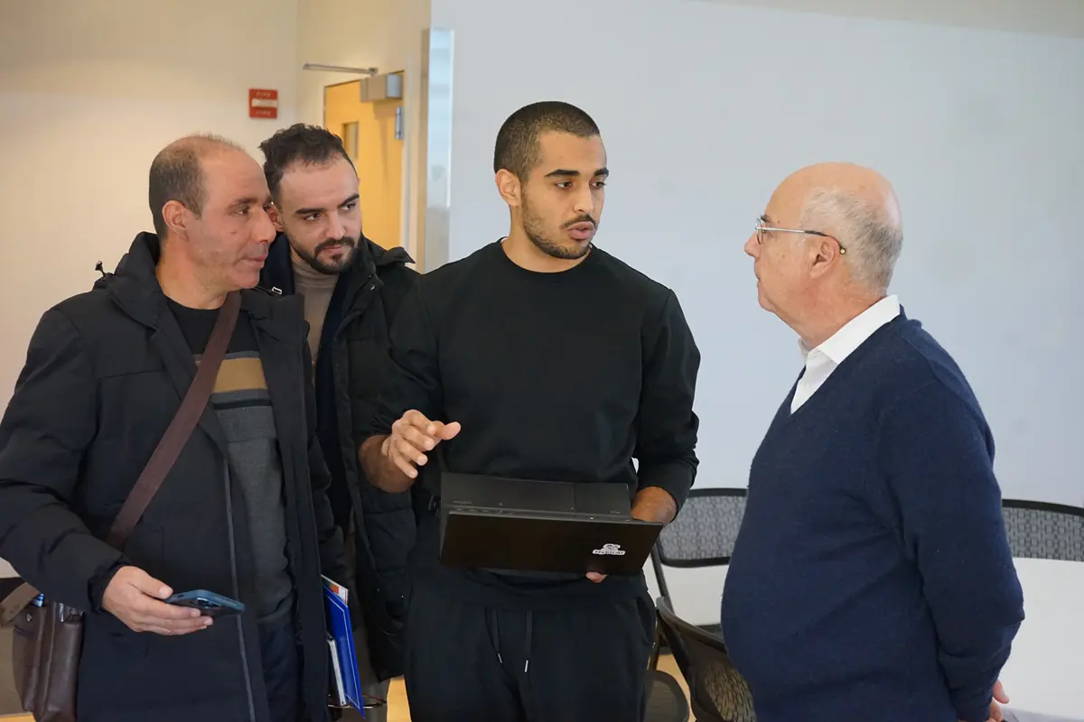 Three men talk to another man who is standing with his hands behind his back.
