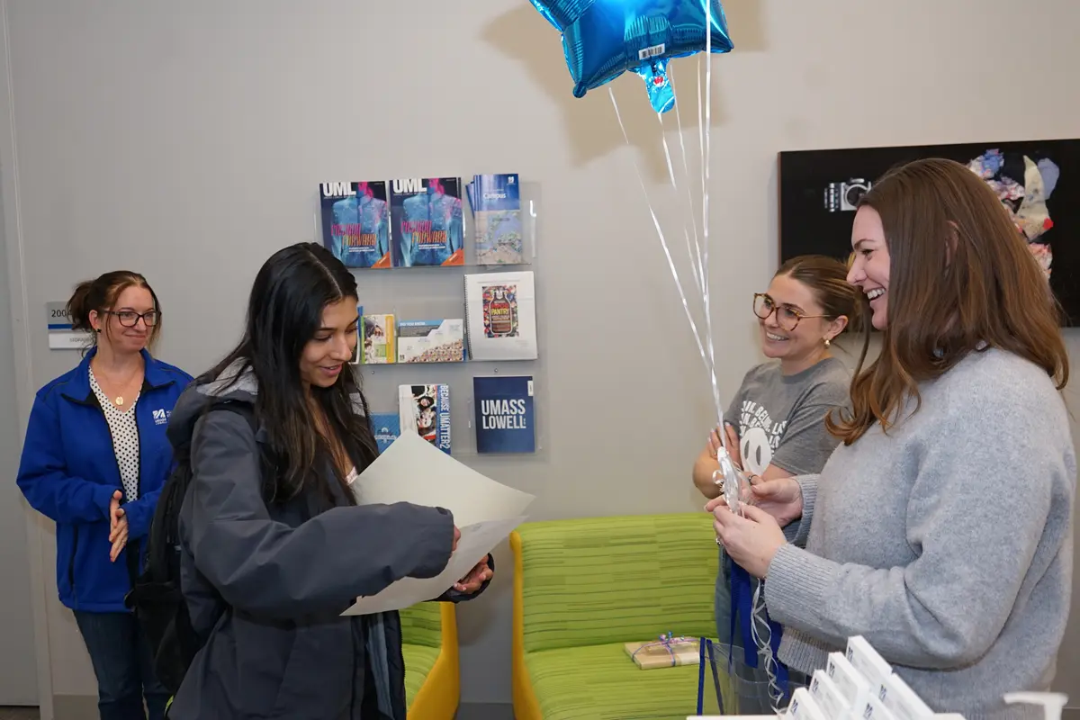 A young woman looks at a certificate in a folder while three other women look on in an office.