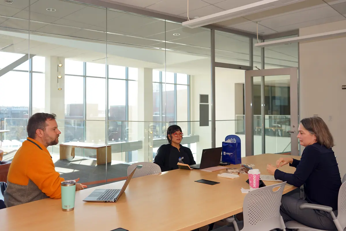 A man and two women sit at a desk in a conference room for a meeting.