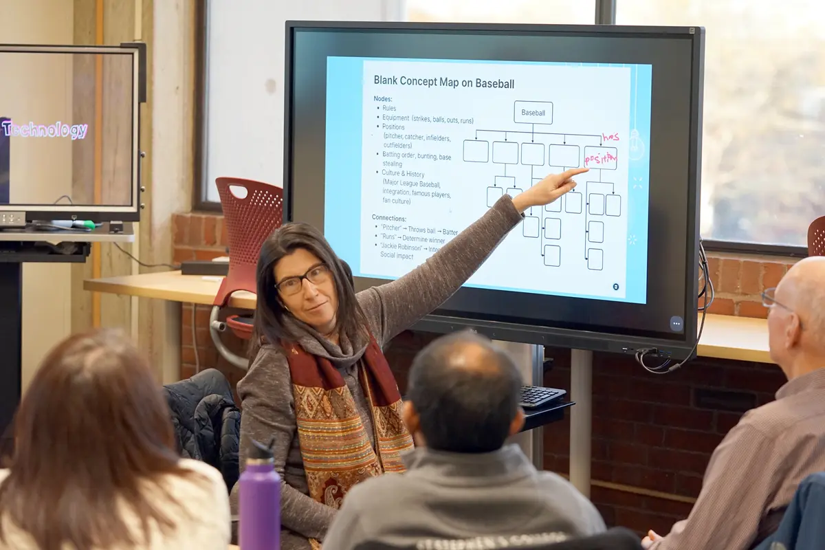 A man in a checkered shirt uses a touch screen monitor in a classroom.