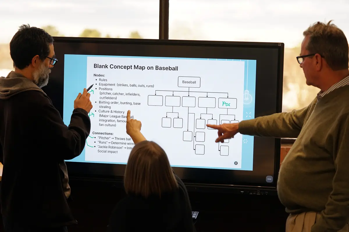 Two men and a woman point to a touch screen monitor that has a concept map on it.