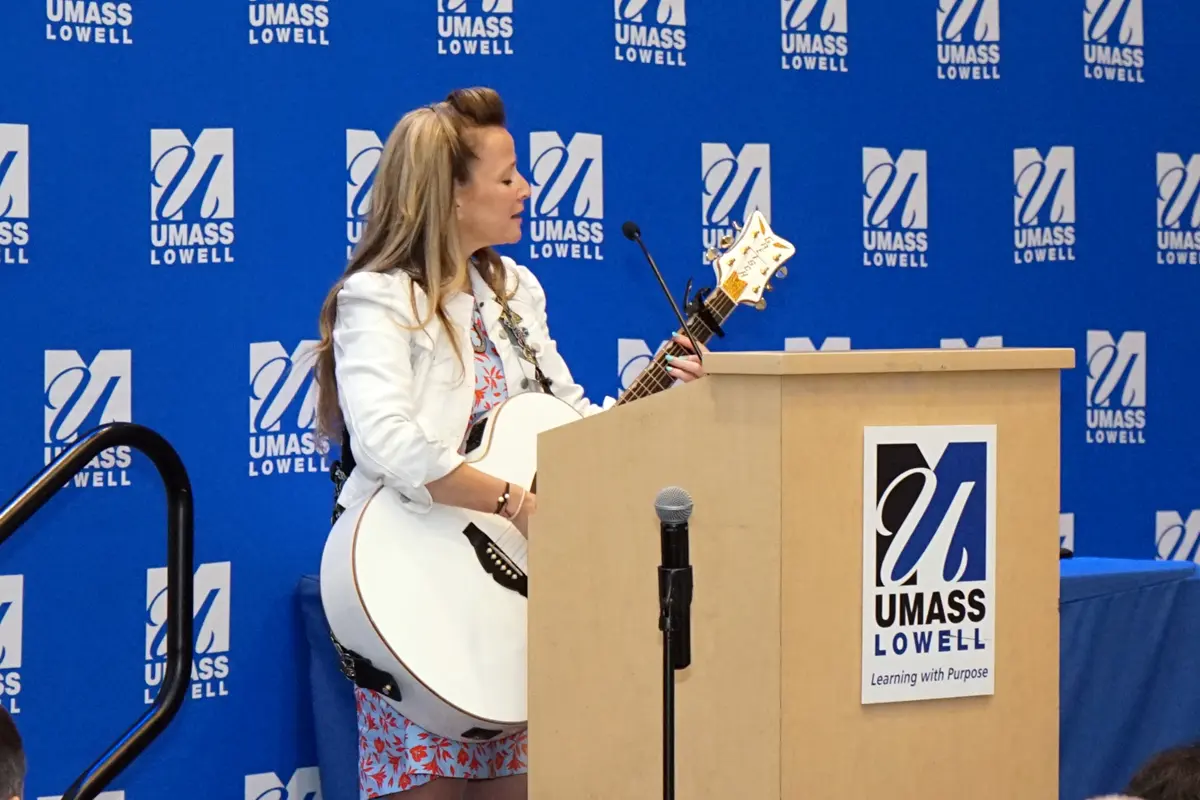 A woman plays an acoustic guitar and sings while standing behind a podium on stage.