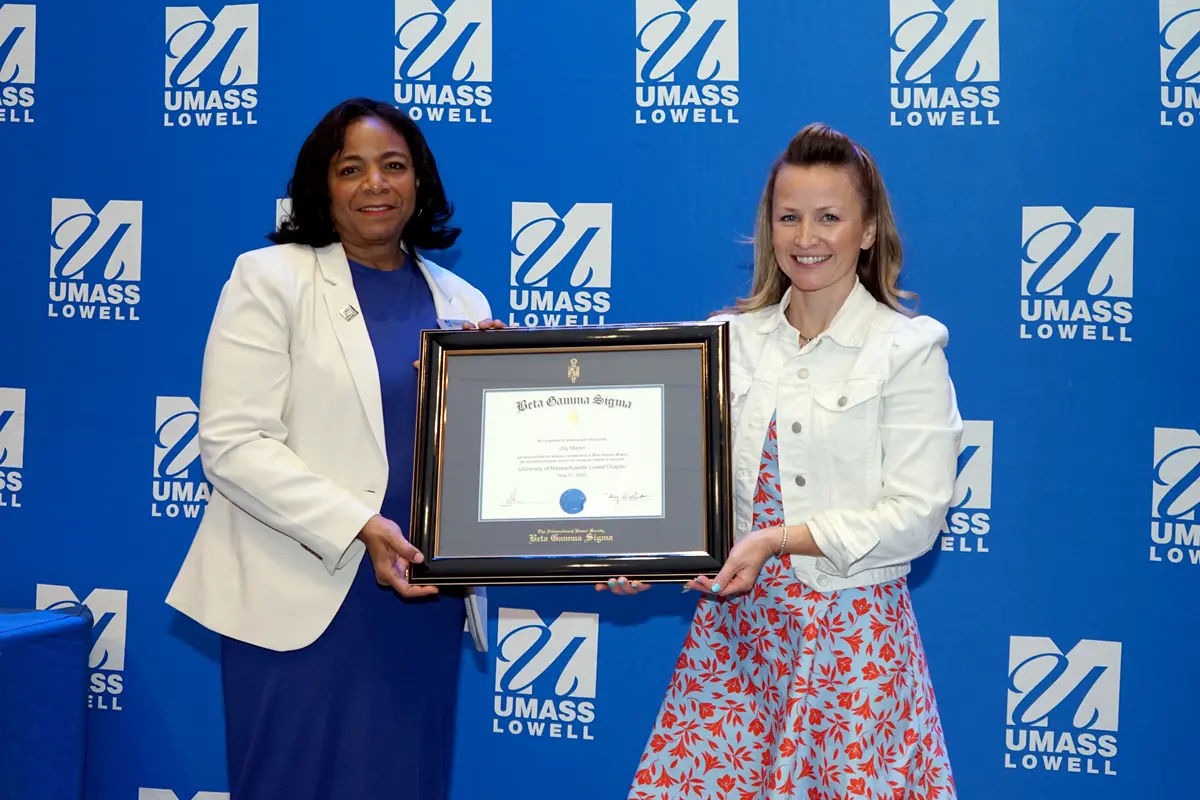 Two women pose for a photo on stage while holding a framed certificate.
