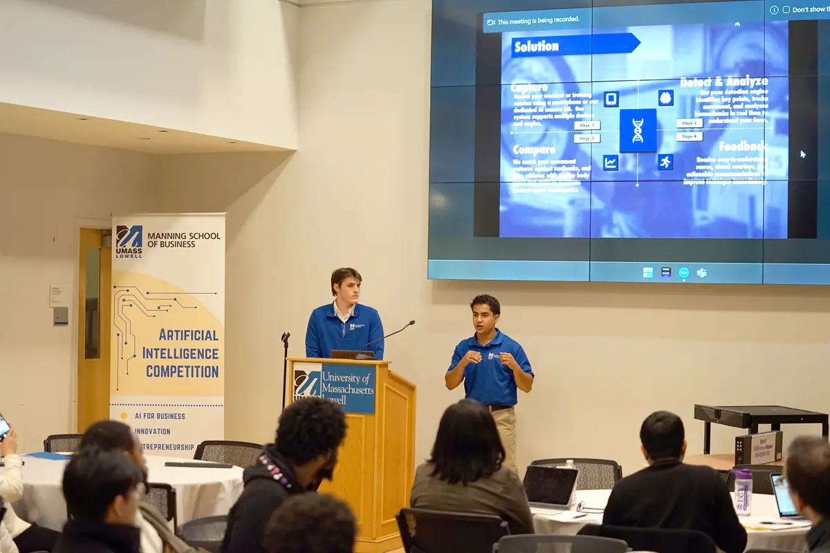Two young men in blue shirts make a presentation from a podium at the front of a room.