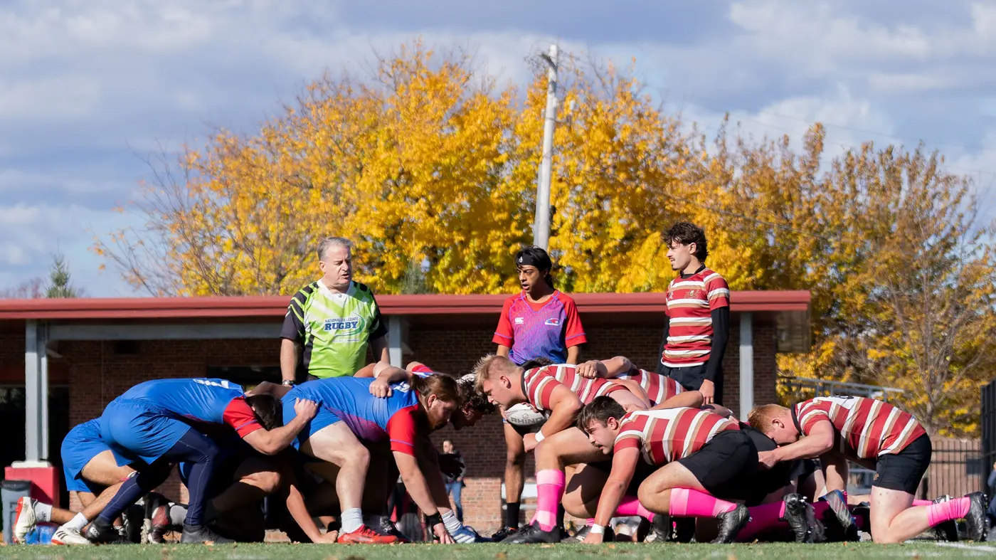 Rugby players line up opposite each other over the ball with a referee standing over