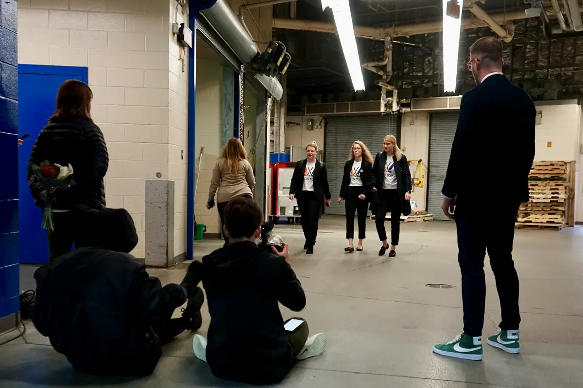 Three people walk into an arena while a group of people watch them.