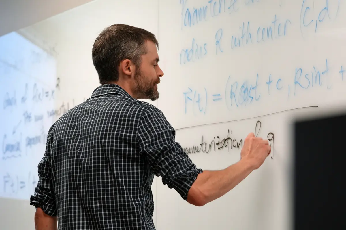 A professor writes a math problem on a whiteboard.