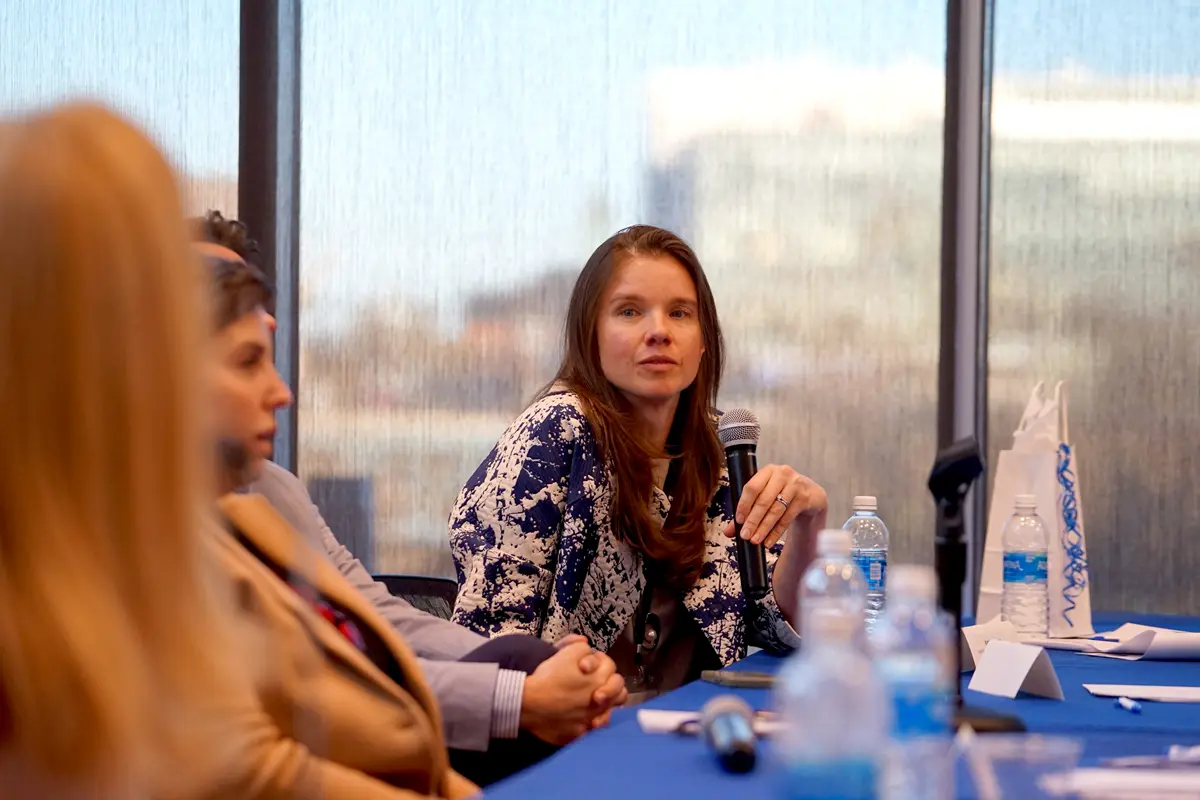 A person holds a microphone while sitting at a table and looking at another person.