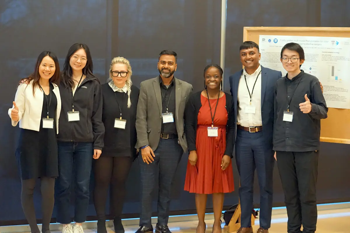 Seven people pose for a photo standing in front of an academic poster. 