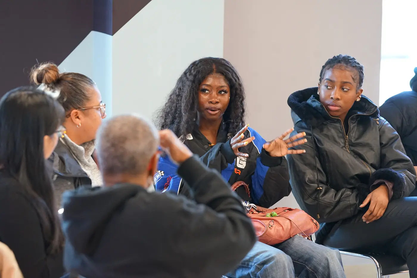 A young woman with long dark hair gestures with her hands while talking to people seated next to her.