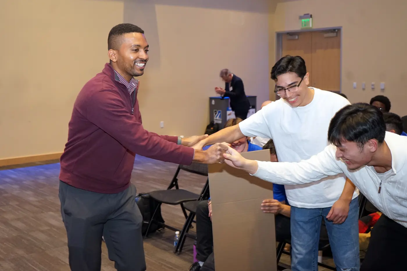 A young man in a maroon shirt slaps hands with two other young men in white shirts.
