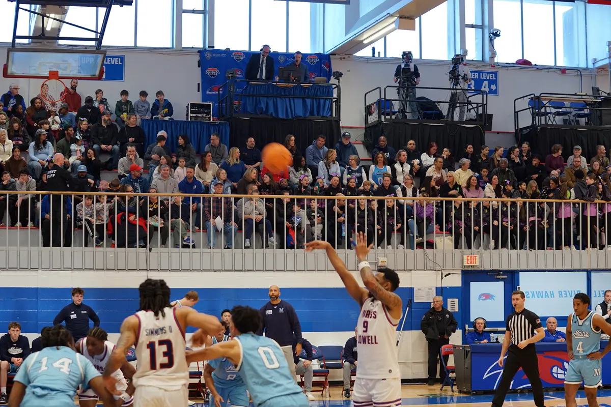 A basketball player shoots a free throw while fans and broadcasters look on in the background.