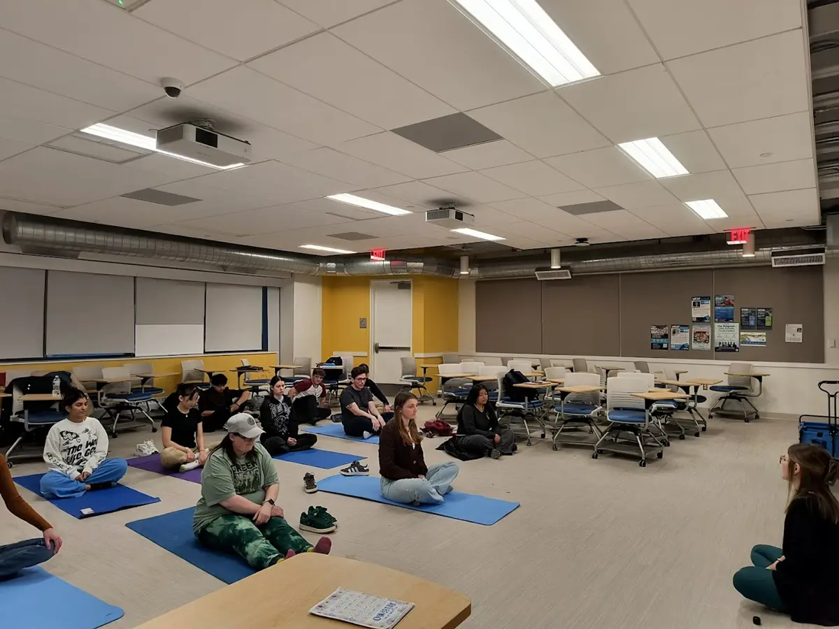 Students sit on yoga mats in classroom surrounded by desks.