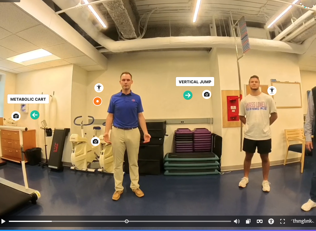 Two people stand inside UMass Lowell's Exercise Science lab with icons and screen tags that say "Metabolic Cart" and "Vertical Jump."