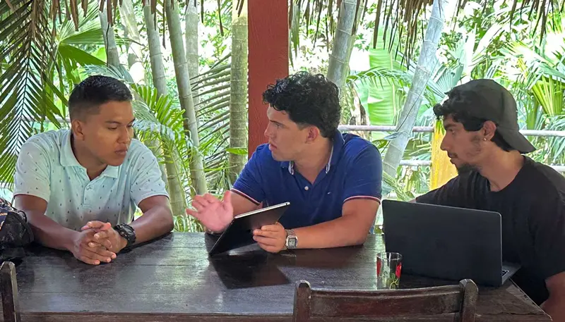 Fidel Castro is seated at a table between two people and showing a tablet computer to one person.