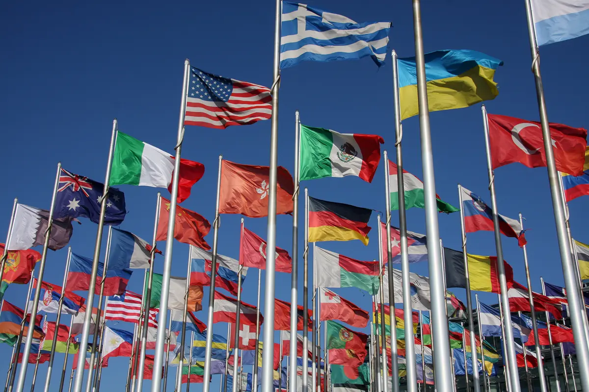 Multiple international flags flying against blue sky background. 