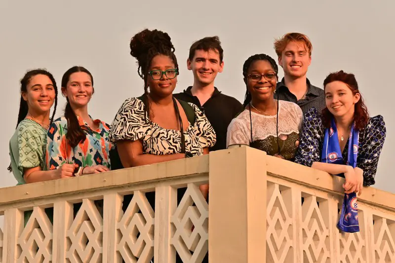 Seven college students pose for a photo while standing on a balcony.