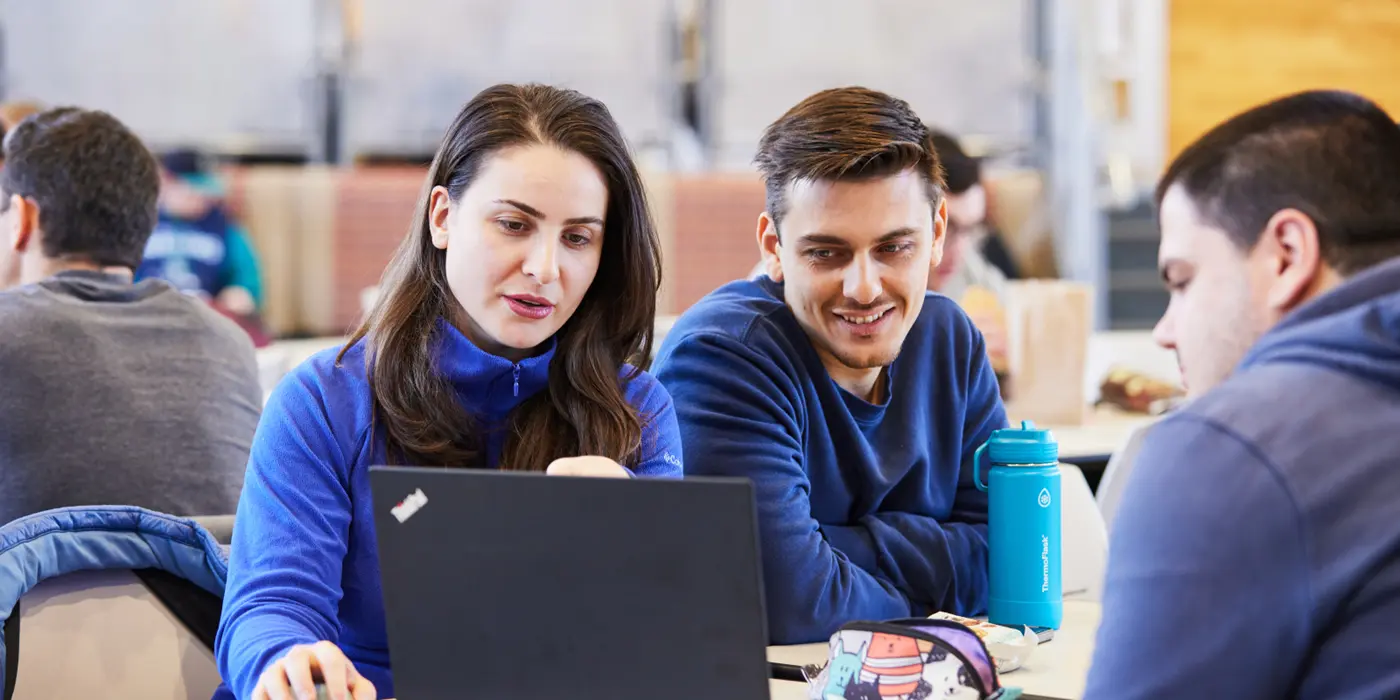 Three students at a table looking together at the display of a laptop computer