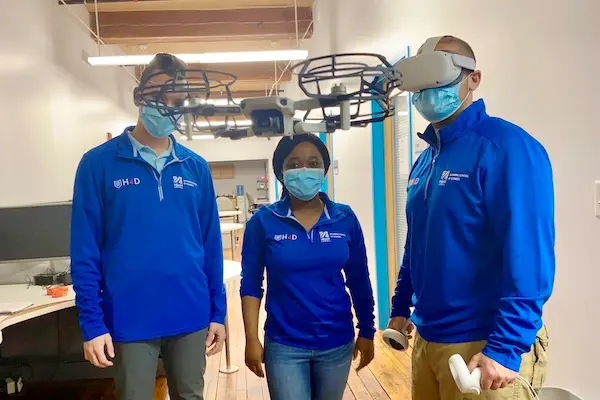 Three Hacking for Defense students pose for a photo with a flying drone