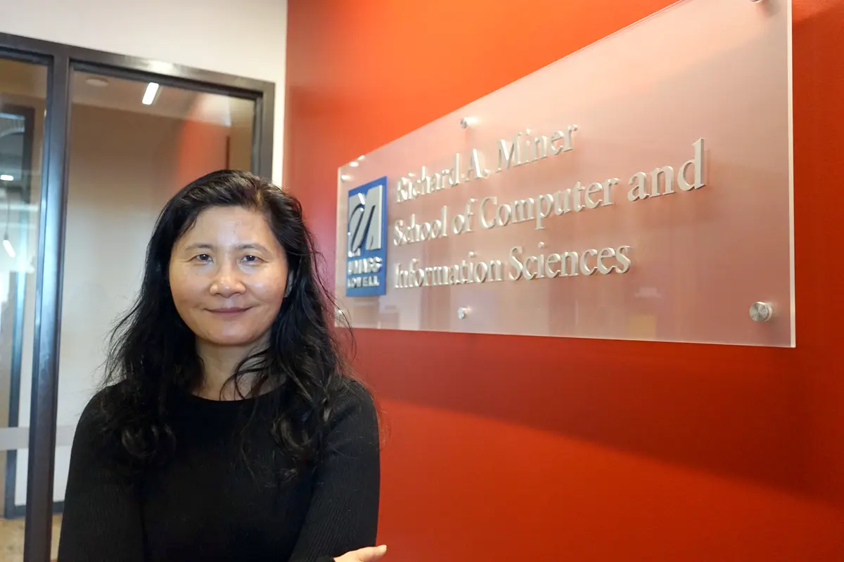 A woman with dark hair poses for a photo next to an orange wall with a glass office sign on it.